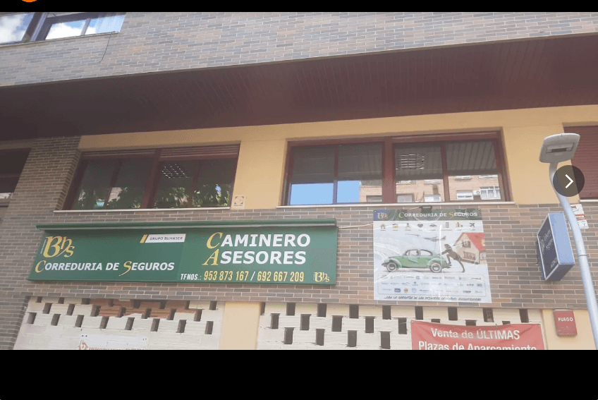 Fachada de ladrillo con letrero de Caminero Asesores Correduría de Seguros y carteles publicitarios.